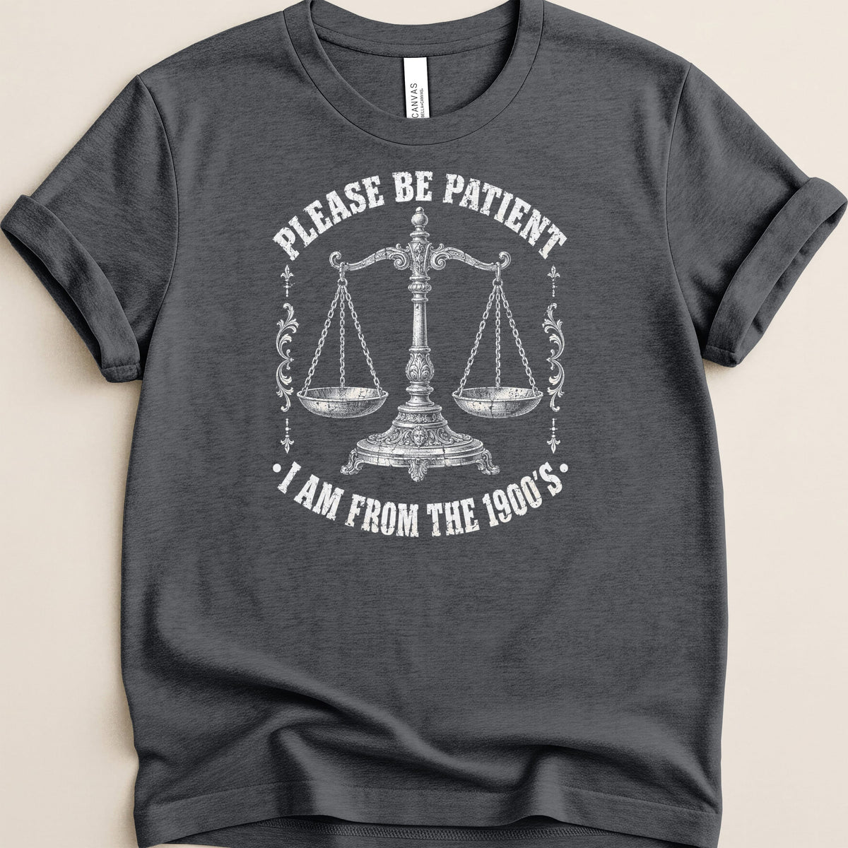 Dark grey t-shirt with white graphic of scales and text "Please be patient. I am from the 1900's."