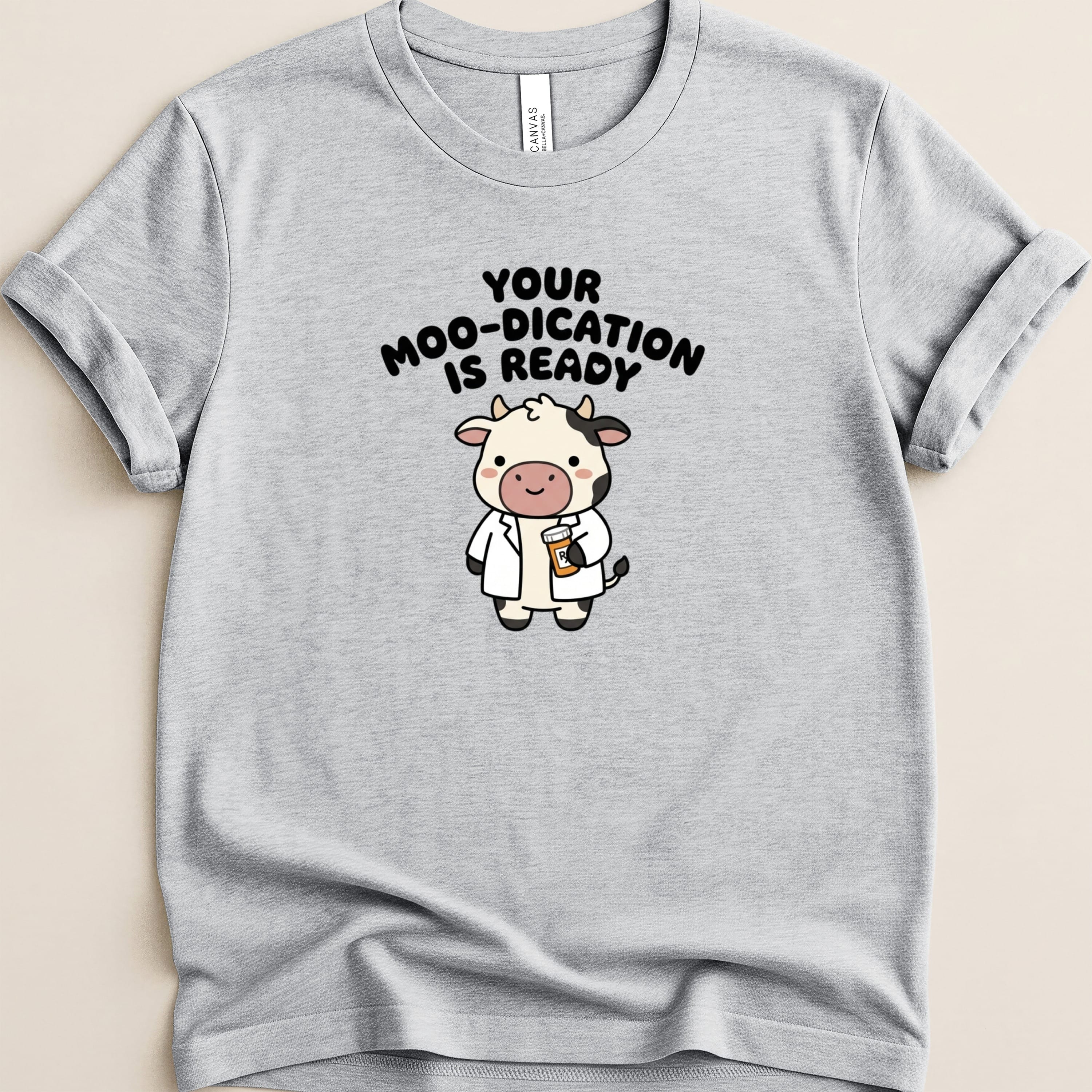 Grey t-shirt with cartoon cow holding a pill bottle, text reads "Your Moo-dication is Ready".