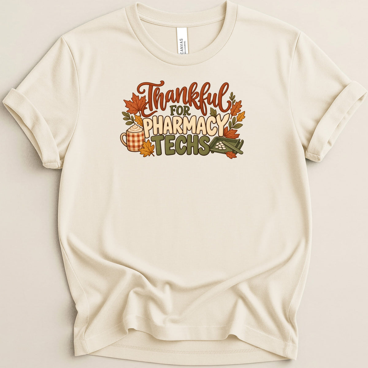 Cream crewneck t-shirt featuring a Thanksgiving graphic with autumn leaves, a coffee mug, and text reading Thankful For Pharmacy Techs.