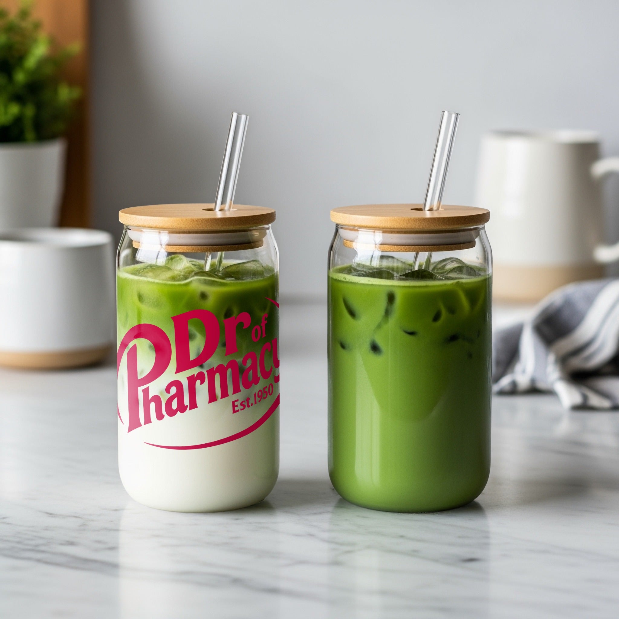 Two glass cups with bamboo lids and straws, one with pink "Dr. of Pharmacy Est. 1950" logo.