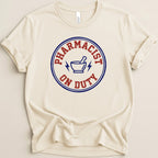 Cream t-shirt with "Pharmacist On Duty" text and lightning bolt symbol.