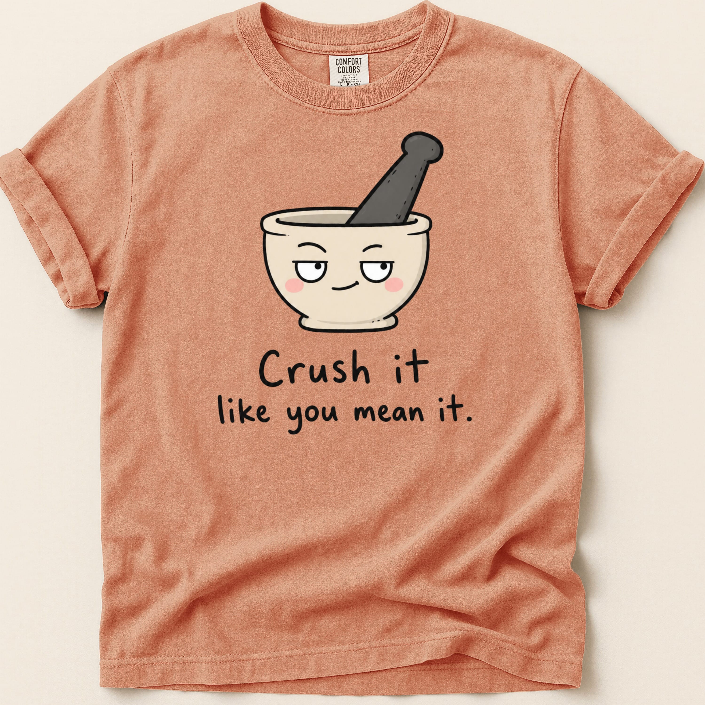 Peach t-shirt with cartoon mortar and pestle and text "Crush it like you mean it."