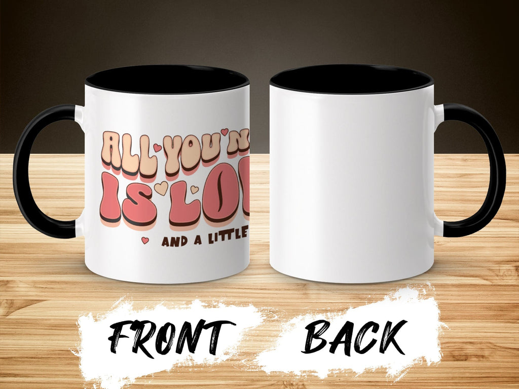 White mug with "All you need is love and a little..." text, black interior and handle.