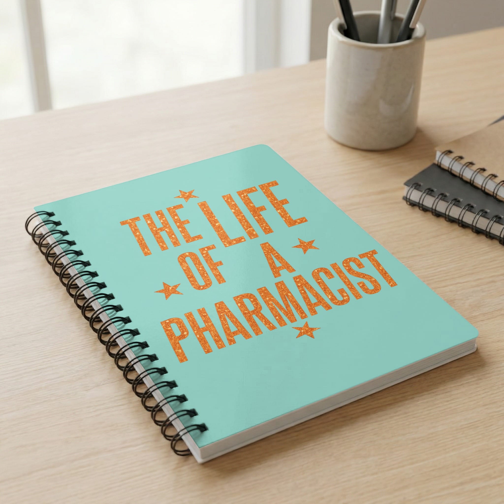Mint green notebook with orange text: "The Life of a Pharmacist".
