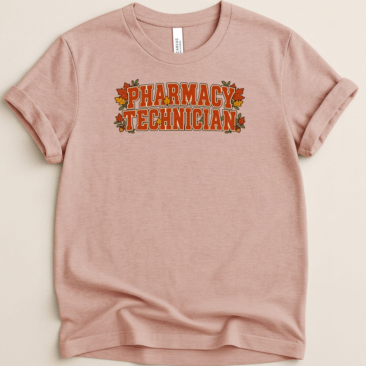 Dusty pink t-shirt featuring the text "PHARMACY TECHNICIAN" in orange block letters surrounded by autumn leaves.