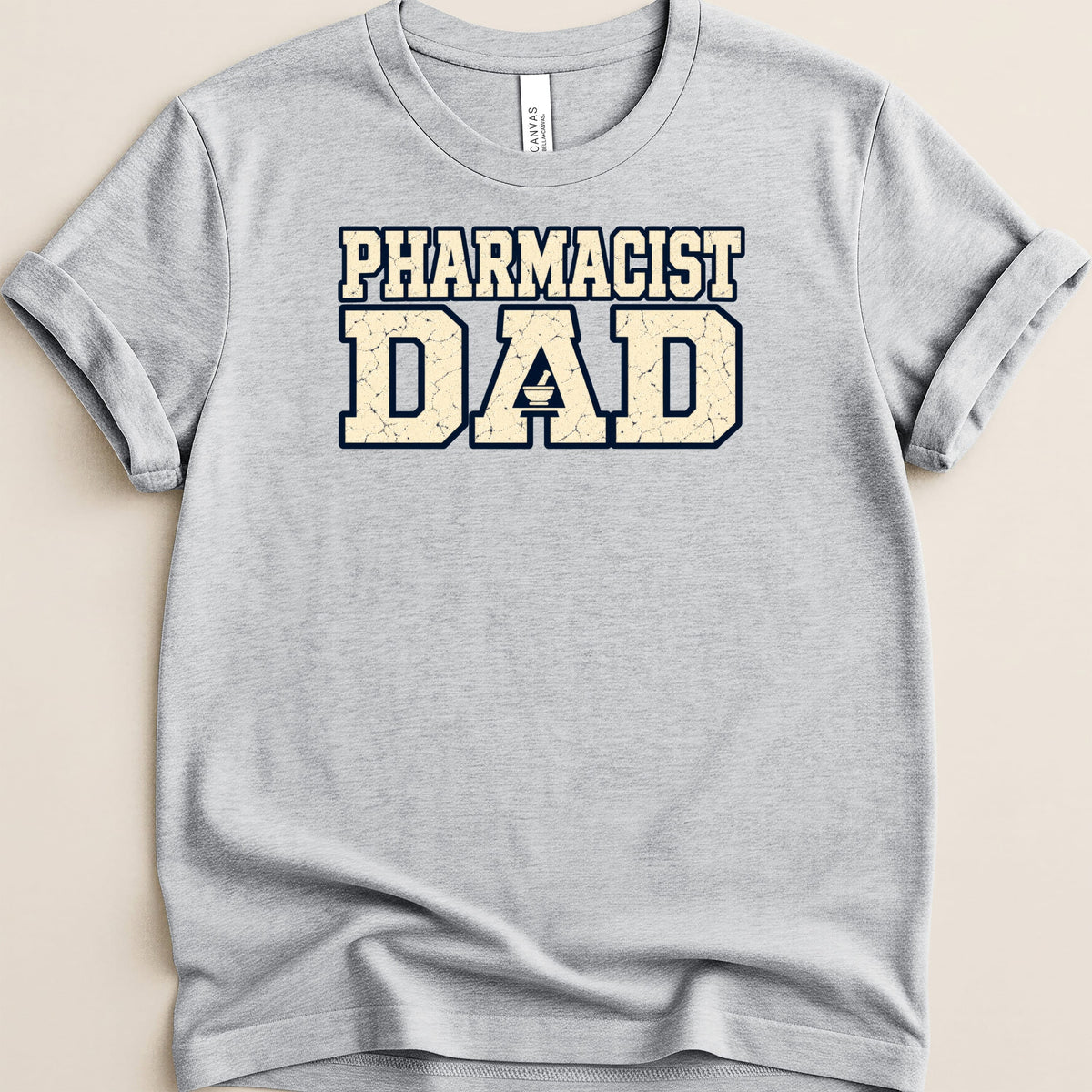 A grey t-shirt featuring distressed blue and cream block text reading PHARMACIST DAD with a mortar and pestle icon.