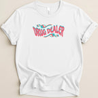 White t-shirt with "DRUG DEALER" text in wavy pink and blue lettering.