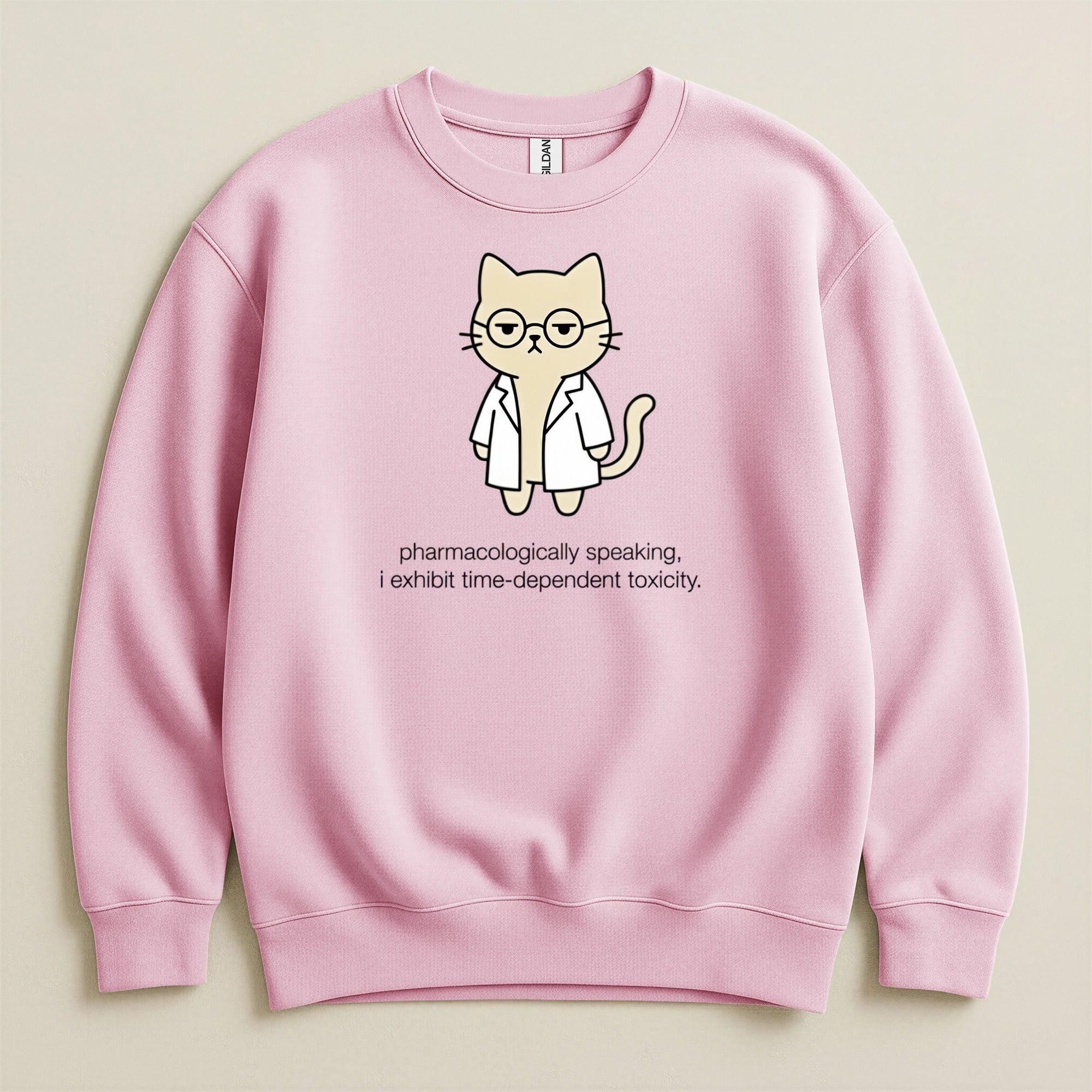 Pink sweatshirt with cartoon cat wearing glasses and lab coat, text reads "pharmacologically speaking, i exhibit time-dependent toxicity."