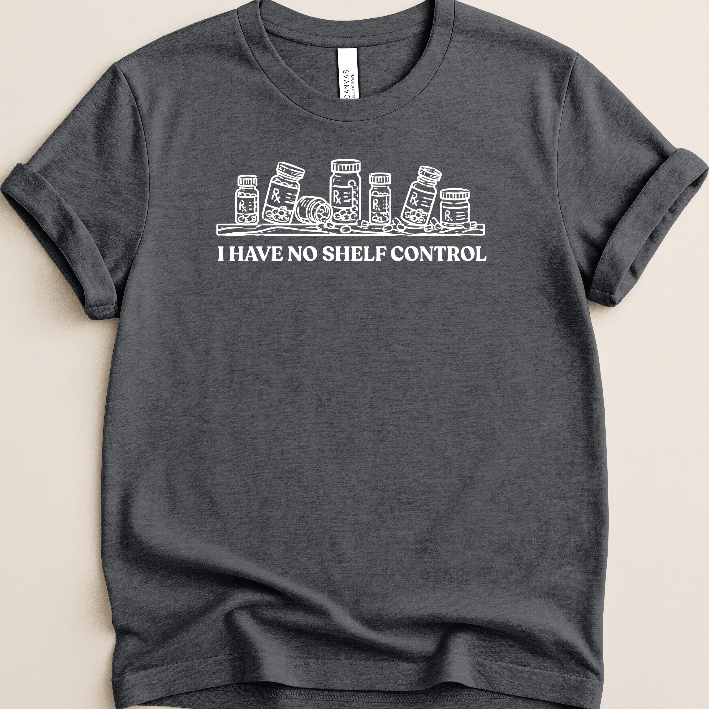Dark gray t-shirt with white line art of prescription bottles and text "I HAVE NO SHELF CONTROL".