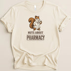 Cream t-shirt with a cartoon squirrel in a lab coat holding medication. Text reads "Nuts About Pharmacy".