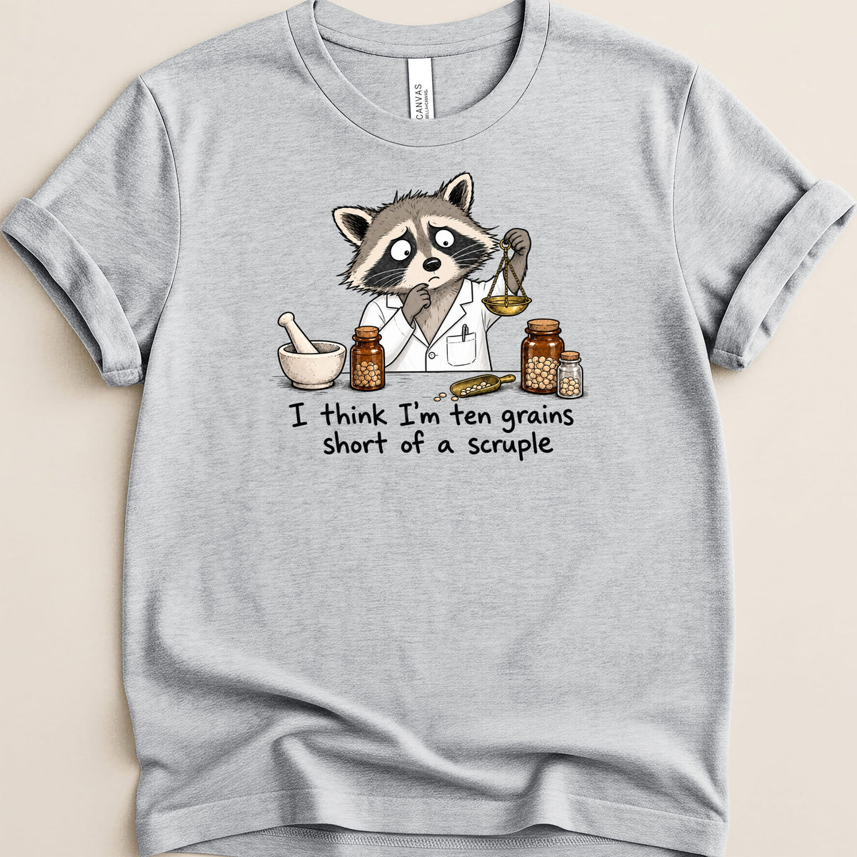 Gray t-shirt with raccoon in lab coat holding balance, "I think I'm ten grains short of a scruple."