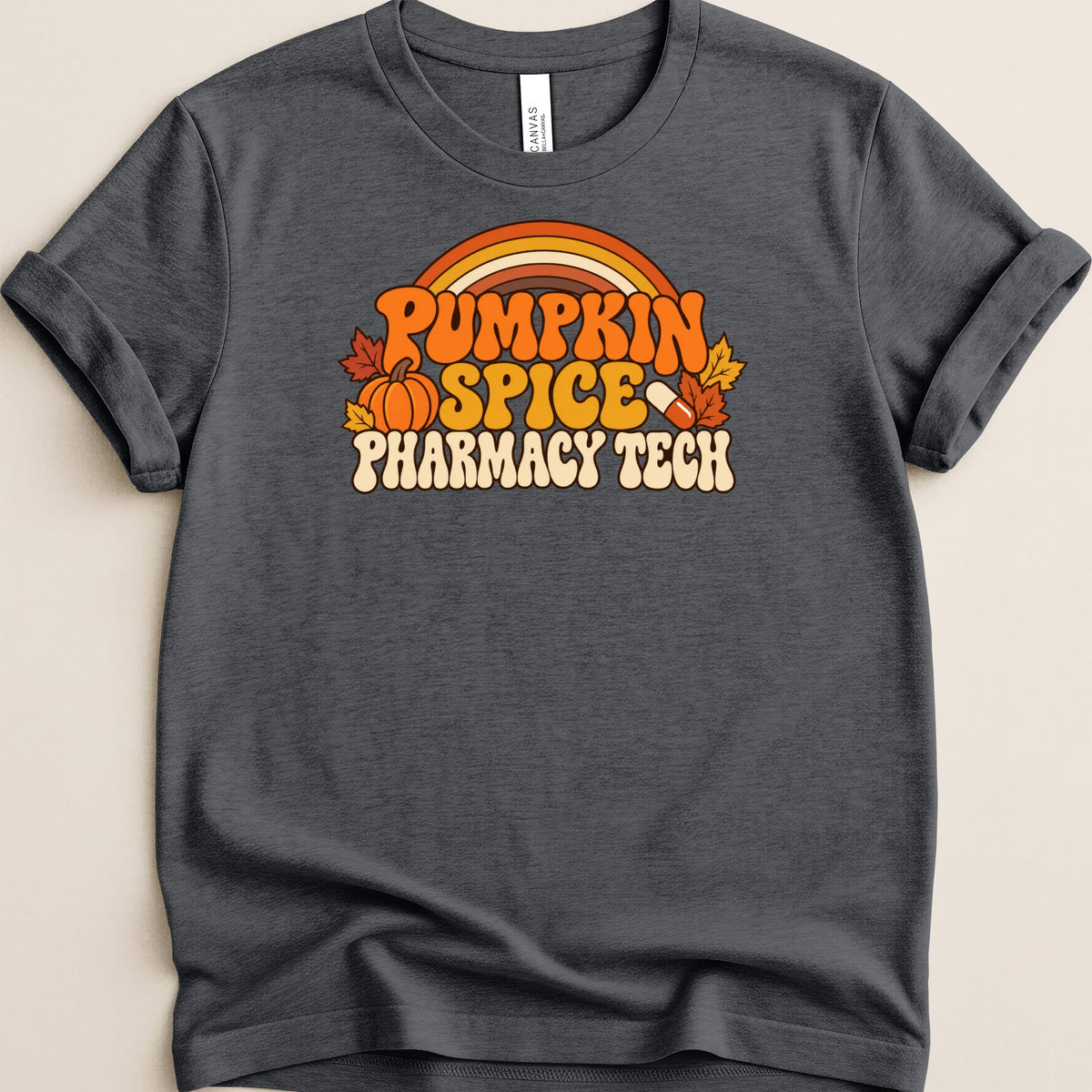 Dark gray t-shirt featuring a retro graphic with orange autumn leaves, a pumpkin, a capsule pill, and text reading Pumpkin Spice Pharmacy Tech.