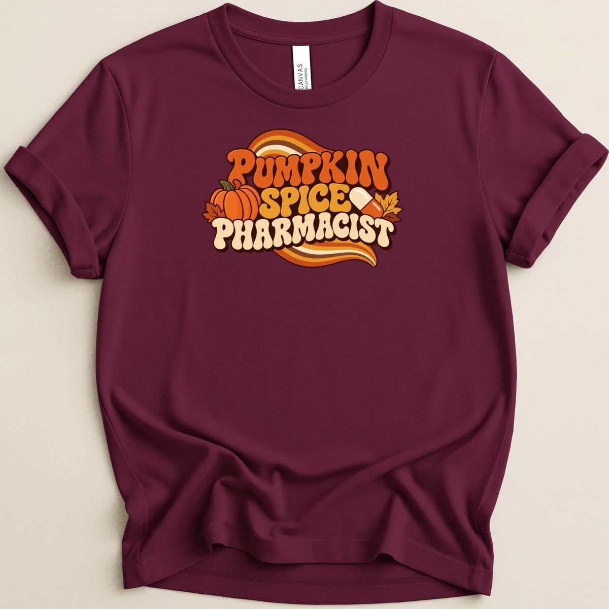 Maroon t-shirt with rolled sleeves featuring a retro design that reads Pumpkin Spice Pharmacist with a pumpkin and pill.