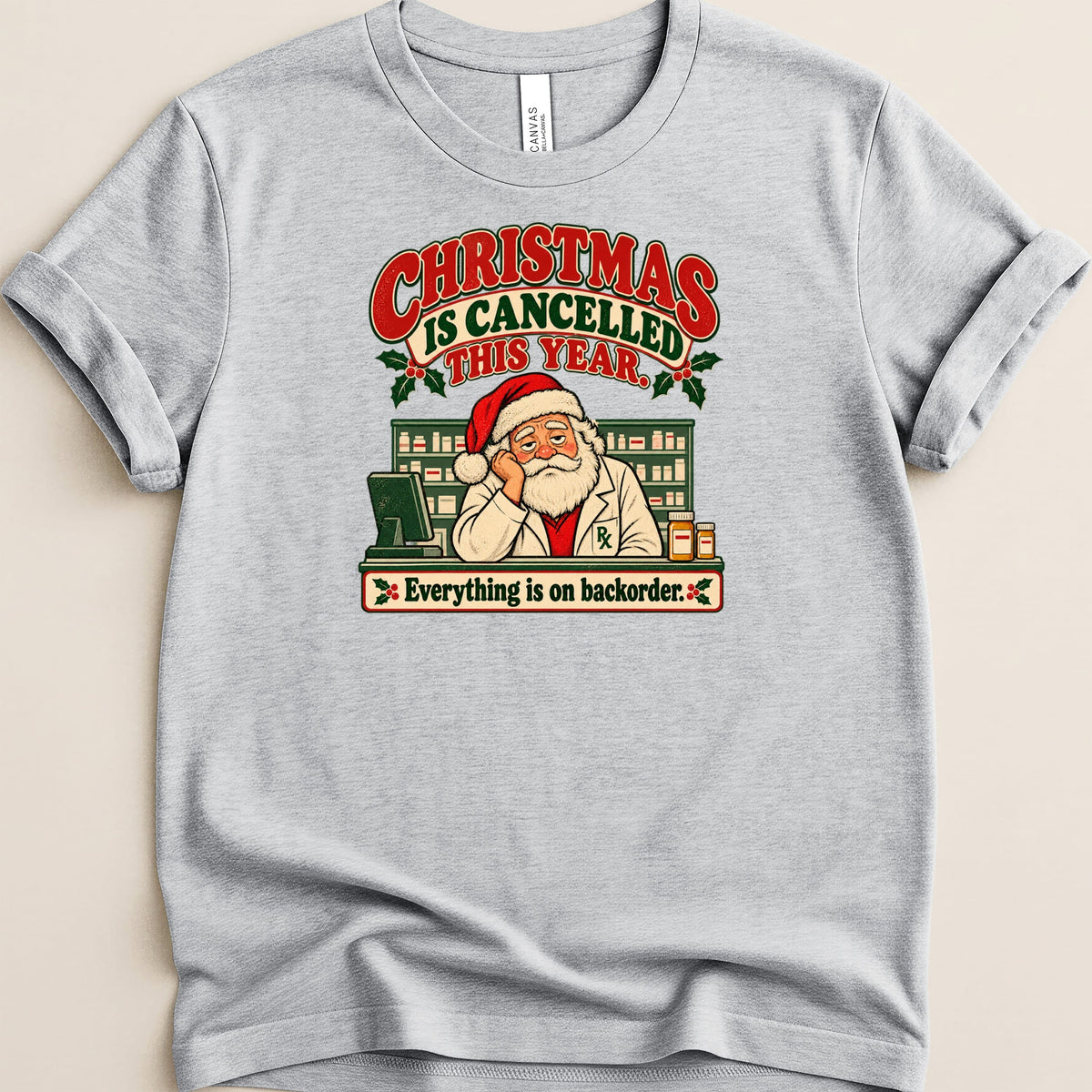A heather gray t-shirt featuring a graphic of Santa working as a pharmacist with text reading Christmas is cancelled this year.