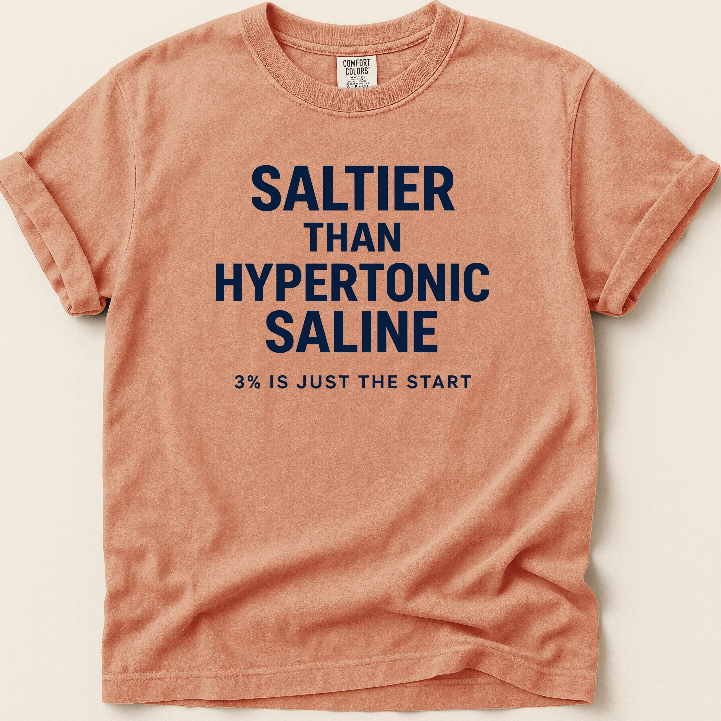 Coral t-shirt with navy blue text reading "SALTIEr THAN HYPERTONIC SALINE 3% IS JUST THE START".