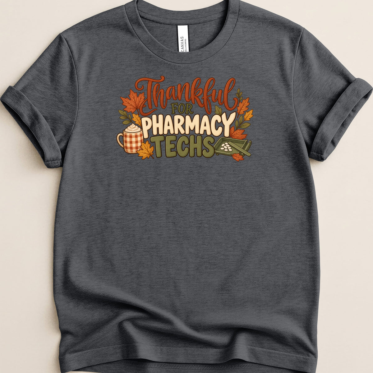A dark gray t-shirt with rolled sleeves features an autumn-themed graphic and text that reads Thankful for Pharmacy Techs.